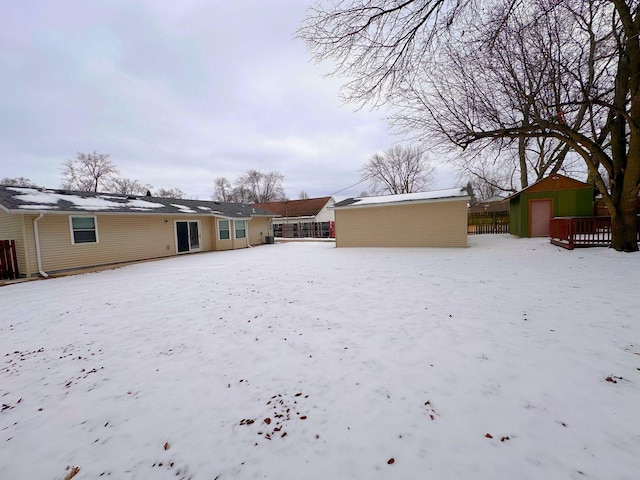 snow covered house with a shed, an outdoor structure, and fence