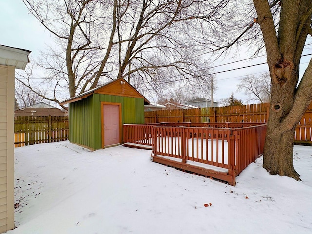 snow covered deck featuring a fenced backyard, a shed, and an outbuilding