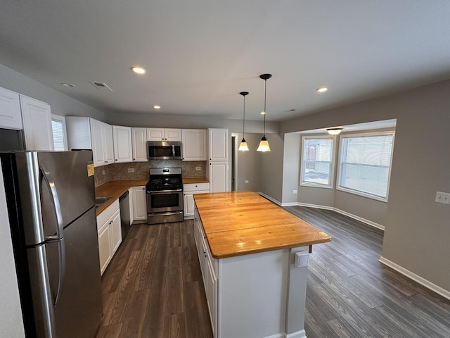 kitchen featuring decorative light fixtures, wooden counters, backsplash, appliances with stainless steel finishes, and white cabinets