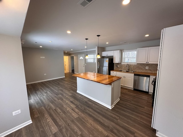 kitchen with butcher block counters, a kitchen island, white cabinets, appliances with stainless steel finishes, and pendant lighting