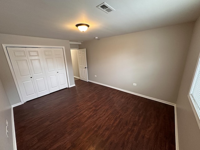 unfurnished bedroom featuring baseboards, a closet, visible vents, and dark wood-type flooring