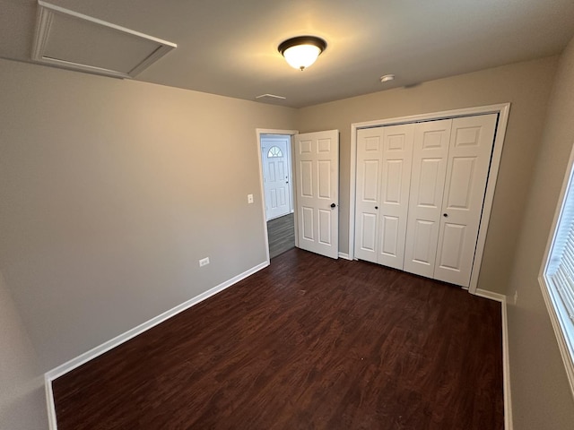 unfurnished bedroom featuring dark wood-style floors, a closet, attic access, and baseboards