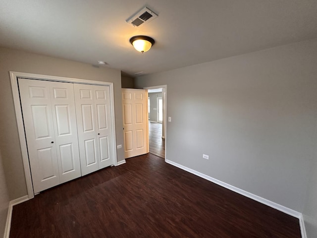 unfurnished bedroom featuring dark wood-style floors, baseboards, visible vents, and a closet