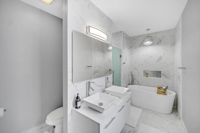 bathroom with marble finish floor, toilet, vanity, and a freestanding tub