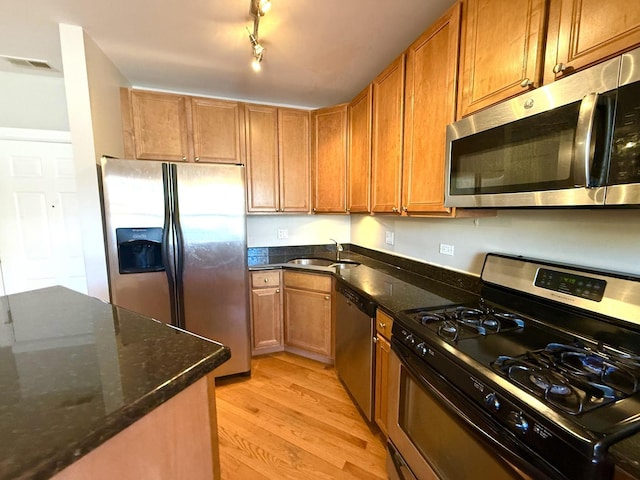 kitchen with light wood finished floors, appliances with stainless steel finishes, brown cabinetry, and a sink