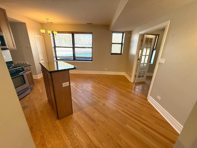 kitchen featuring dark countertops, appliances with stainless steel finishes, light wood-style floors, pendant lighting, and a wealth of natural light