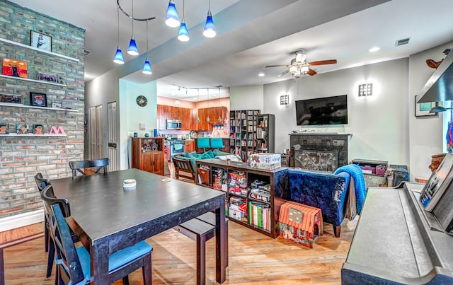 dining room featuring light wood finished floors, visible vents, a glass covered fireplace, ceiling fan, and track lighting