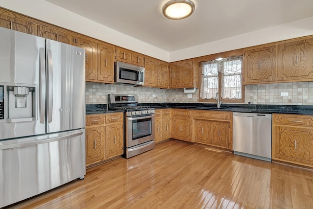 kitchen with appliances with stainless steel finishes, sink, backsplash, and light wood-type flooring