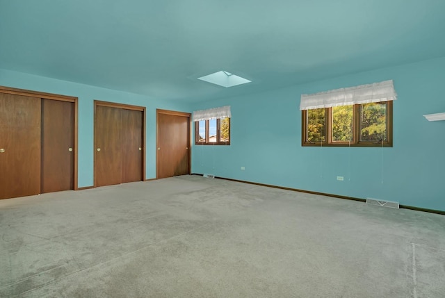 unfurnished bedroom featuring carpet, a skylight, and two closets