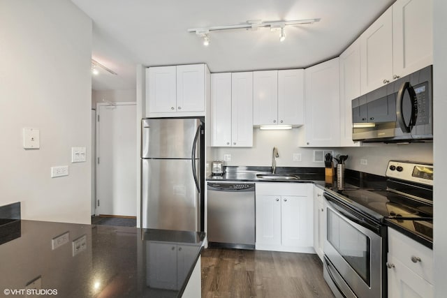 kitchen with white cabinets, dark countertops, dark wood-style floors, stainless steel appliances, and a sink