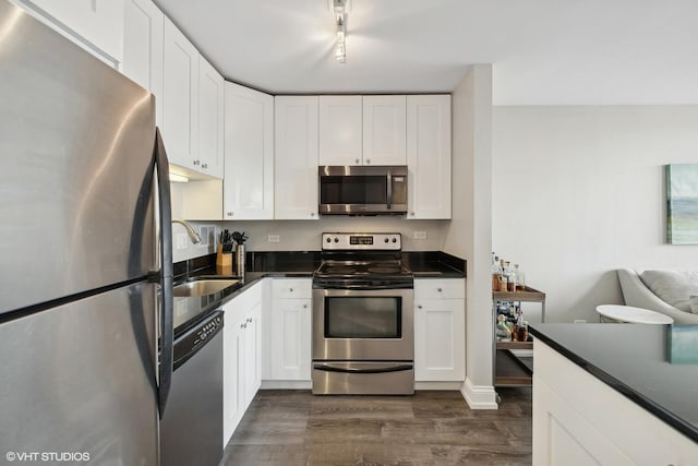 kitchen featuring stainless steel appliances, dark countertops, white cabinetry, and a sink