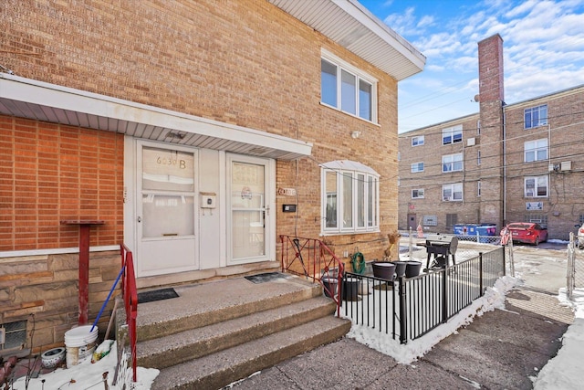 doorway to property featuring brick siding and fence