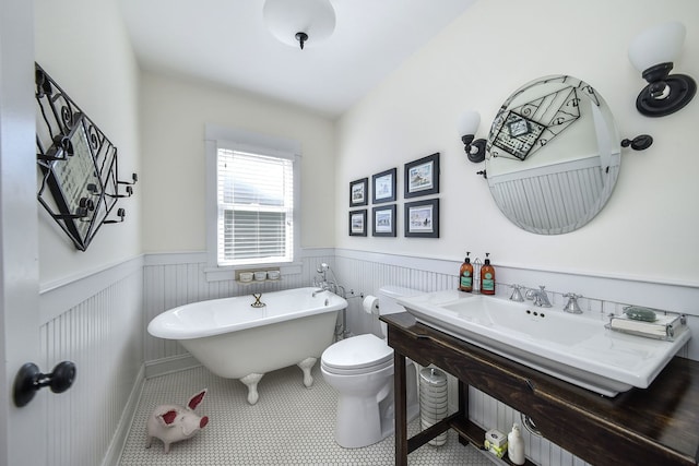 full bath featuring toilet, wainscoting, a freestanding tub, and tile patterned flooring