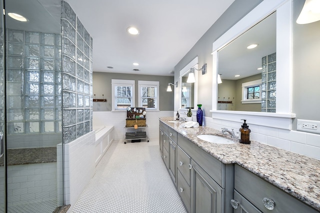 full bath featuring tile walls, double vanity, a sink, tile patterned flooring, and a bath