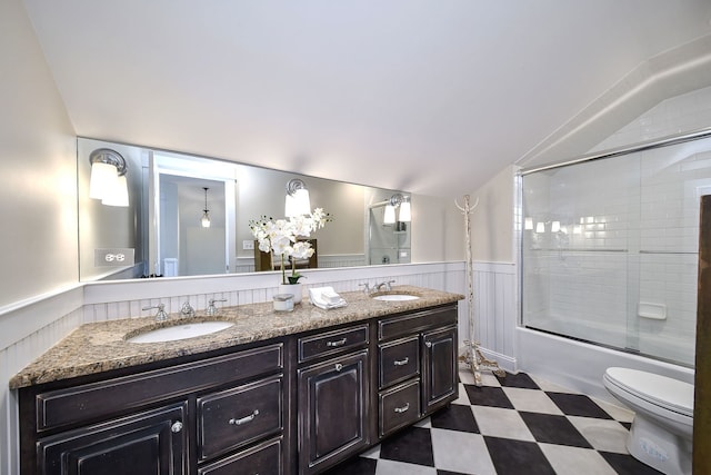 bathroom featuring a wainscoted wall, double vanity, vaulted ceiling, and a sink