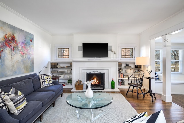 living room featuring wood finished floors, baseboards, a brick fireplace, decorative columns, and crown molding