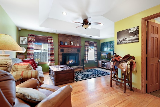 living area with a ceiling fan, a tray ceiling, a fireplace, and hardwood / wood-style flooring