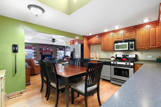 kitchen with light wood finished floors, a fireplace, stainless steel appliances, and decorative backsplash