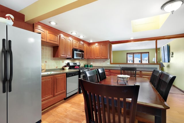 kitchen with stainless steel appliances, brown cabinets, light wood-style flooring, and decorative backsplash