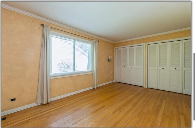 unfurnished bedroom with light wood-style flooring, ornamental molding, baseboards, and multiple closets