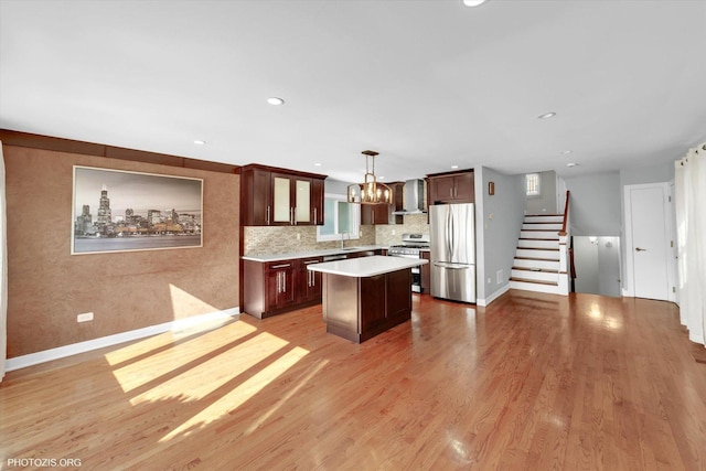 kitchen with stainless steel appliances, a kitchen island, light countertops, wall chimney exhaust hood, and decorative light fixtures