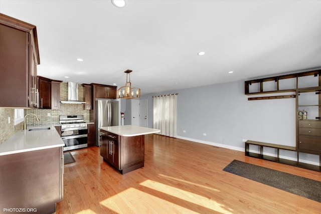 kitchen featuring wall chimney exhaust hood, a kitchen island, appliances with stainless steel finishes, light countertops, and a sink