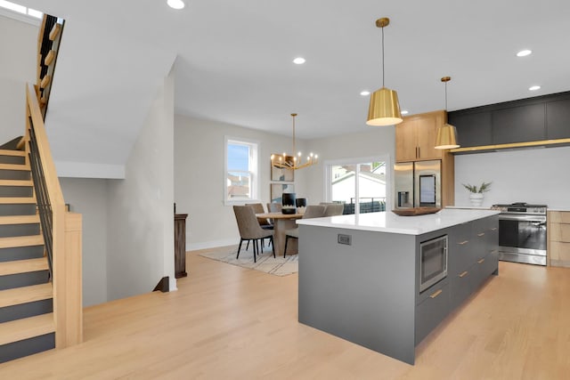 kitchen with decorative light fixtures, gray cabinetry, stainless steel appliances, a center island, and light hardwood / wood-style floors