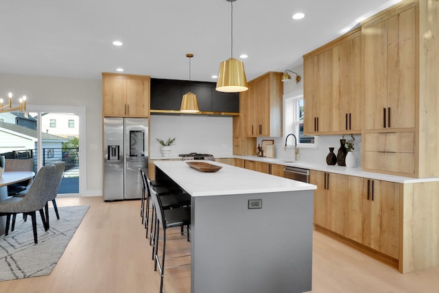 kitchen featuring appliances with stainless steel finishes, a center island, light hardwood / wood-style floors, pendant lighting, and a breakfast bar