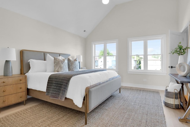 bedroom featuring high vaulted ceiling, light hardwood / wood-style flooring, and multiple windows