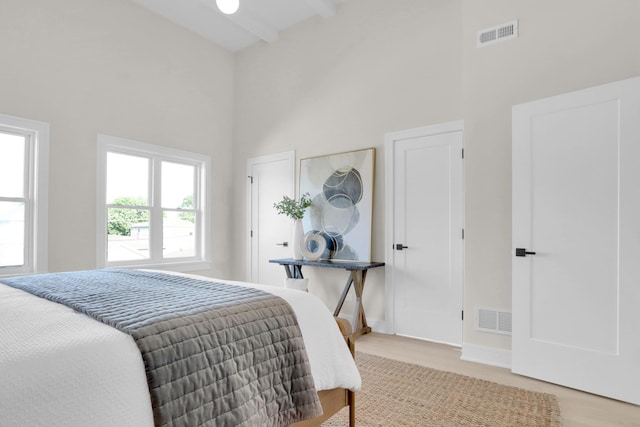 bedroom featuring beam ceiling, a towering ceiling, and light hardwood / wood-style flooring