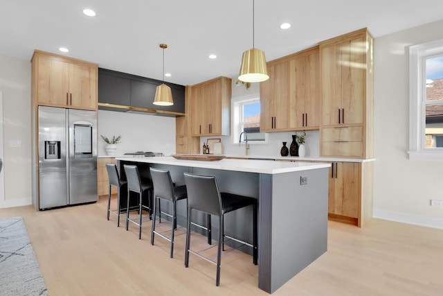 kitchen with light brown cabinets, a center island, hanging light fixtures, and appliances with stainless steel finishes