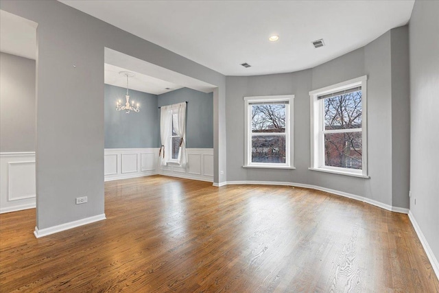 unfurnished room with visible vents, an inviting chandelier, and wood finished floors