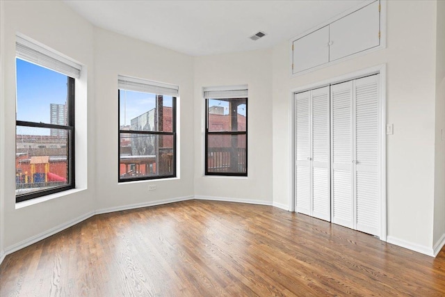 unfurnished bedroom with a view of city, wood finished floors, visible vents, baseboards, and a closet