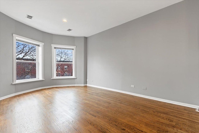 empty room featuring baseboards, visible vents, and wood finished floors