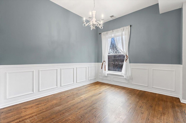 unfurnished dining area featuring a wainscoted wall, dark wood-type flooring, and a chandelier