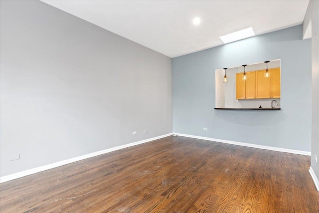 spare room with dark wood-type flooring, baseboards, and a skylight