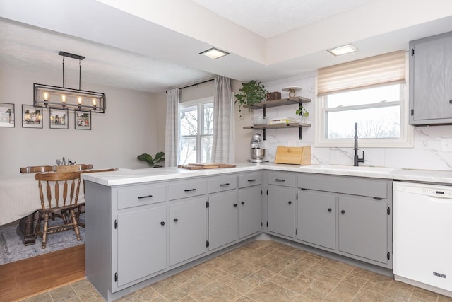 kitchen with a sink, gray cabinetry, light countertops, pendant lighting, and dishwasher