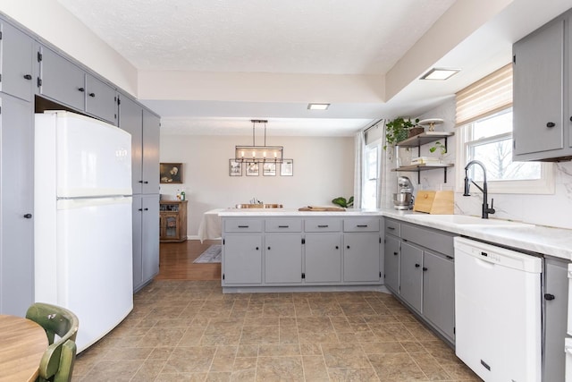 kitchen with a sink, pendant lighting, light countertops, gray cabinetry, and white appliances