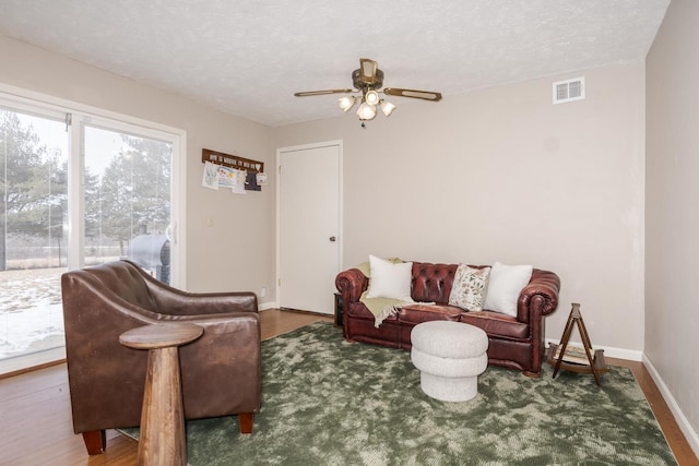 living room with baseboards, visible vents, a textured ceiling, and wood finished floors