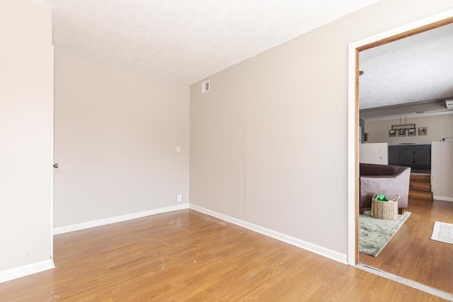 unfurnished room with a textured ceiling, baseboards, wood finished floors, and visible vents