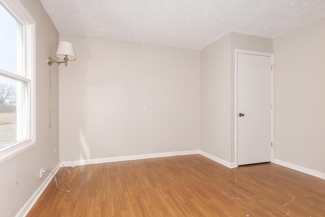 unfurnished room featuring light wood-style flooring, baseboards, and a textured ceiling