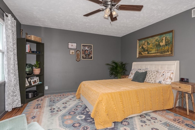 bedroom featuring a ceiling fan, wood finished floors, baseboards, visible vents, and a textured ceiling