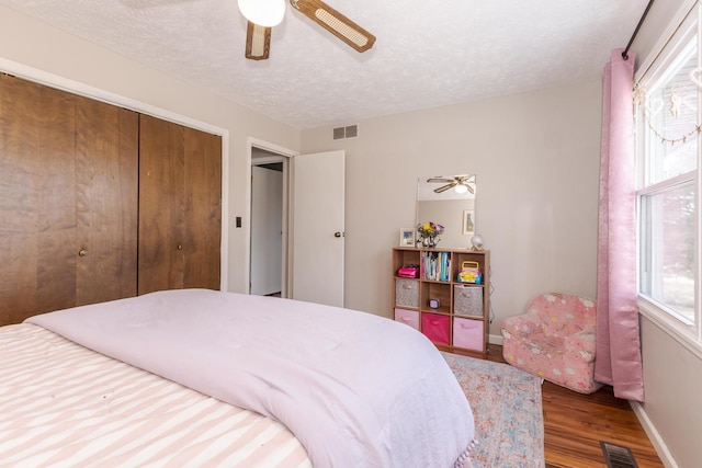 bedroom with baseboards, visible vents, a textured ceiling, and wood finished floors