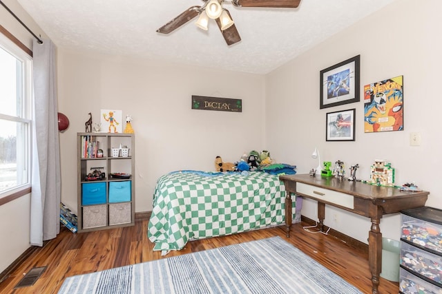 bedroom with a ceiling fan, wood finished floors, baseboards, visible vents, and a textured ceiling