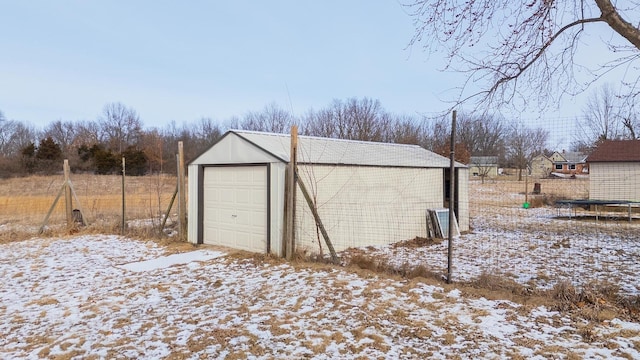 snow covered garage featuring fence, a trampoline, and a garage