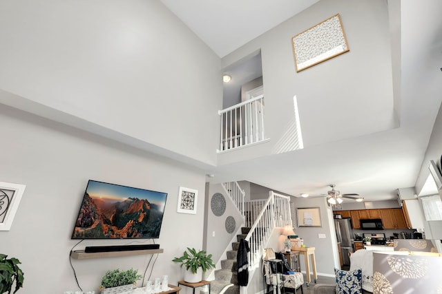 living room featuring a high ceiling, stairway, a ceiling fan, and baseboards