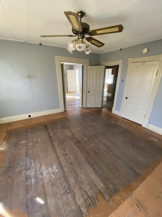 empty room featuring dark wood-type flooring, a ceiling fan, and baseboards