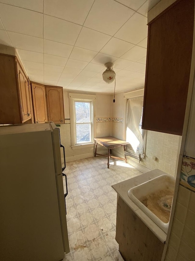 kitchen with brown cabinetry, freestanding refrigerator, and light floors