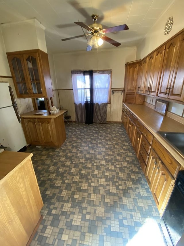 kitchen with a wainscoted wall, brown cabinetry, freestanding refrigerator, ceiling fan, and dishwasher