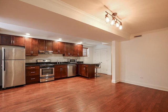 kitchen with dark countertops, stainless steel appliances, ornamental molding, visible vents, and under cabinet range hood